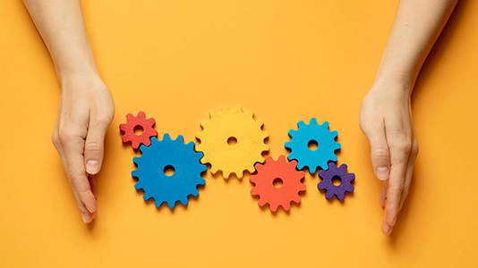 Hands arranging colorful gears on a yellow background, representing the process of tuning and optimizing a Google Ads campaign