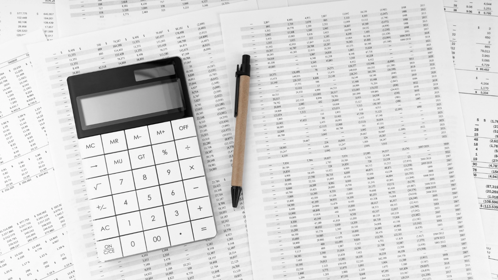 Calculator and pen placed on printed financial spreadsheets with rows of numbers, representing ad budget calculation and cost analysis